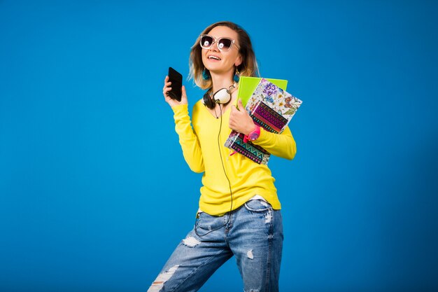 Mulher bonita e jovem hippie segurando livros e olhando para o smartphone