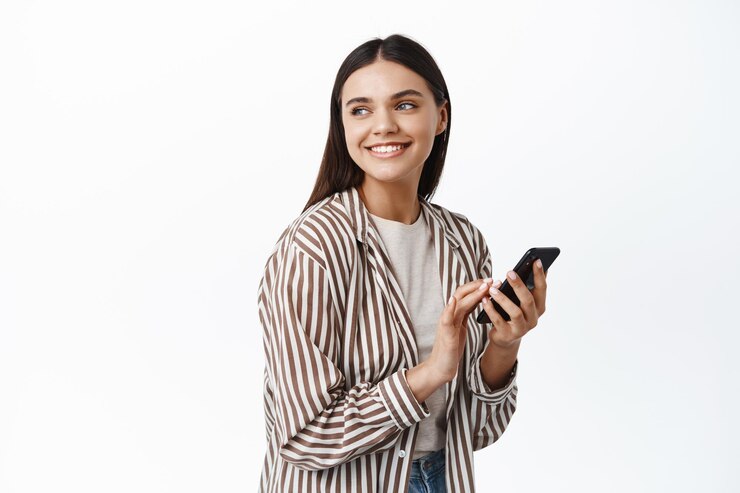 Foto grátis mulher bonita e moderna segurando um smartphone e olhando para trás para o logotipo do espaço de cópia, sorrindo satisfeito