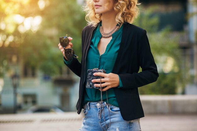 Mulher bonita elegante em jeans e jaqueta andando na rua com bolsinha, estilo elegante, tendências da moda de primavera
