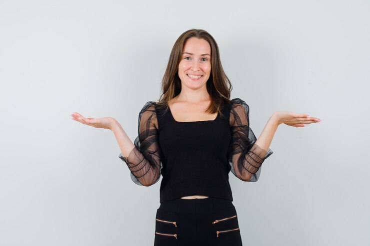 Foto grátis mulher bonita em blusa preta com as palmas das mãos abertas para o lado e parecendo feliz