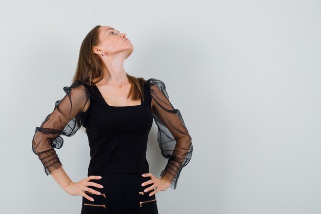 Mulher bonita em blusa preta olhando para longe, segurando as mãos na cintura e parecendo ofendida