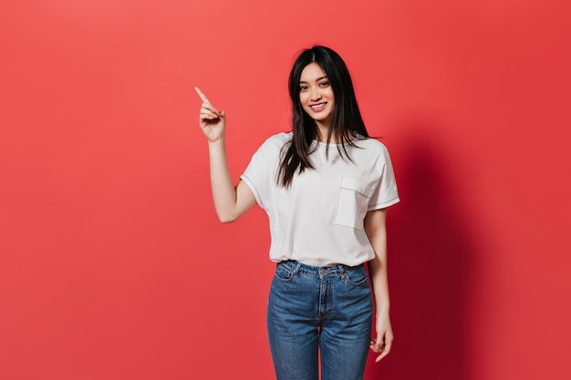 Mulher bonita em calças jeans mostra o dedo para colocar o texto na parede vermelha