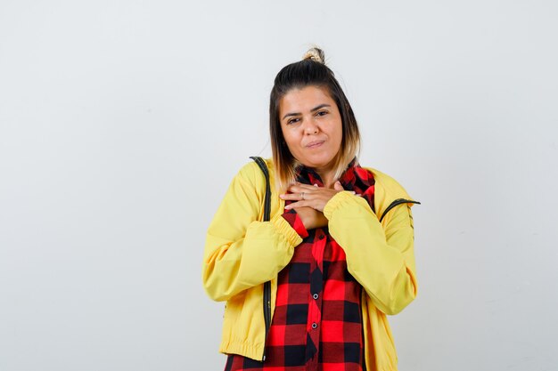 Mulher bonita em camisa, jaqueta de mãos dadas no peito e olhando agradecida, vista frontal.