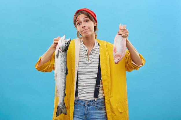 Mulher bonita em capa de chuva posando contra uma parede azul com peixe fresco