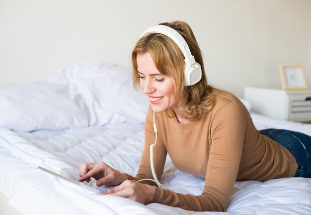 Mulher bonita em fones de ouvido, ouvindo música na cama