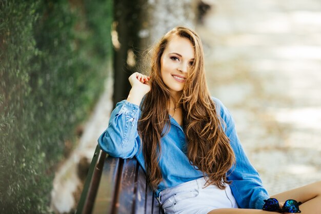 Mulher bonita em óculos de sol sorrindo relaxando no banco do parque