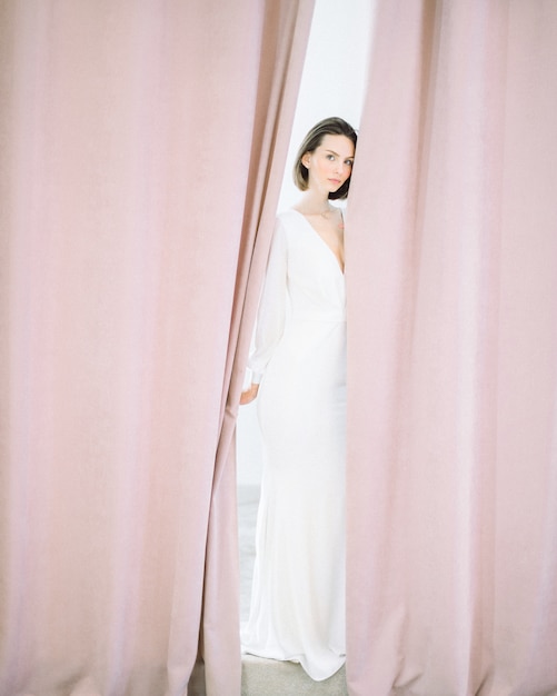 Mulher bonita em pé e olhando no quarto pérola vestido longo branco.