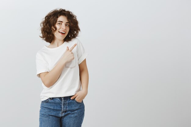 Mulher bonita em roupas casuais apontando o dedo no canto superior direito, convidando para verificar o produto