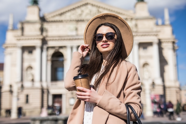 Mulher bonita em roupas casuais de outono posando na cidade com uma xícara de café nas mãos dela