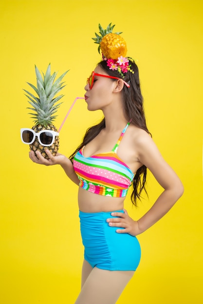 Foto grátis mulher bonita em um maiô segurando um abacaxi poses em amarelo