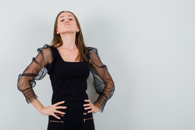 Mulher bonita em uma blusa preta olhando para a câmera, segurando as mãos na cintura dela e parecendo satisfeita