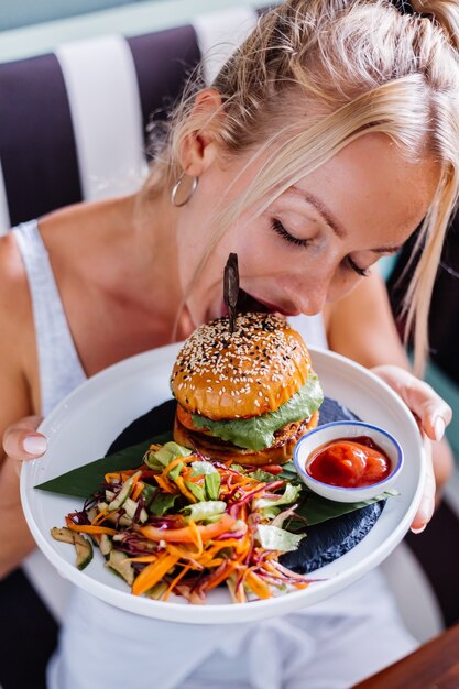 Mulher bonita europeia com fome de hambúrguer suculento em café de verão