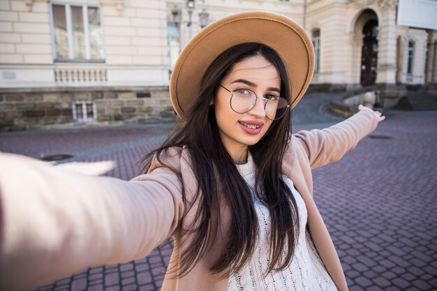 Mulher bonita faz selfie em seu novo smartphone ao ar livre na cidade em dia de sol