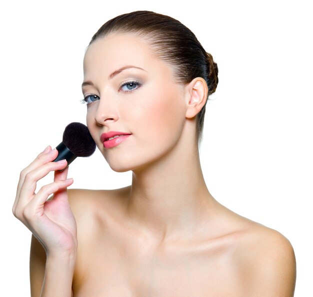 Mulher bonita fazendo maquiagem no rosto com escova cosmética.