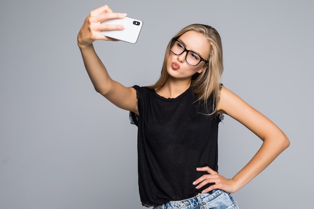 Mulher bonita feliz fazendo selfie no telefone sobre fundo cinza.