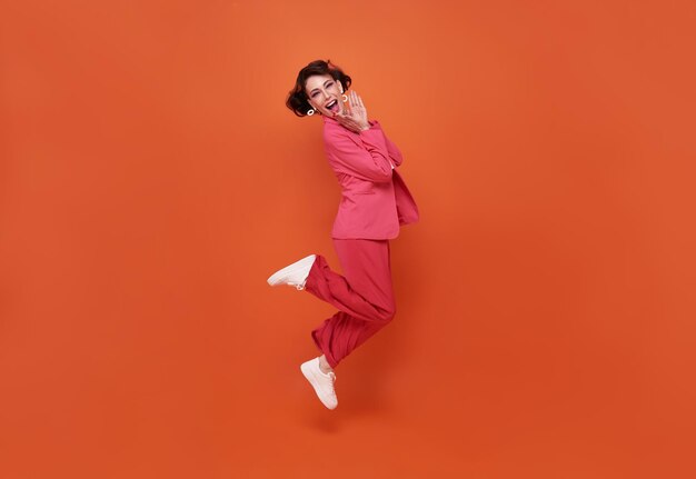 Mulher bonita feliz sorrindo e pulando enquanto comemora o sucesso isolado sobre fundo laranja