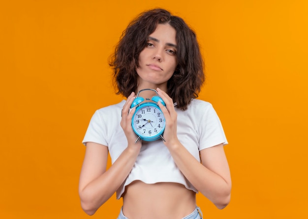 Foto grátis mulher bonita jovem confiante segurando o despertador na parede laranja isolada com espaço de cópia