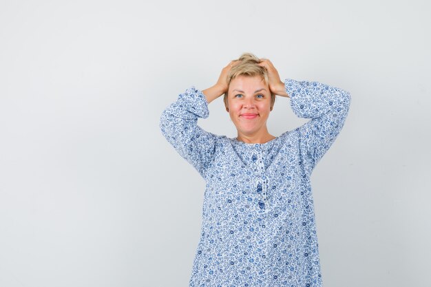 Mulher bonita na blusa estampada, segurando a cabeça com as mãos e olhando fofa, vista frontal.