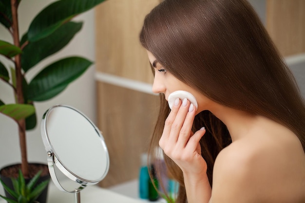 Mulher bonita no banheiro, fazendo procedimentos cosméticos para cuidados com a pele facial.