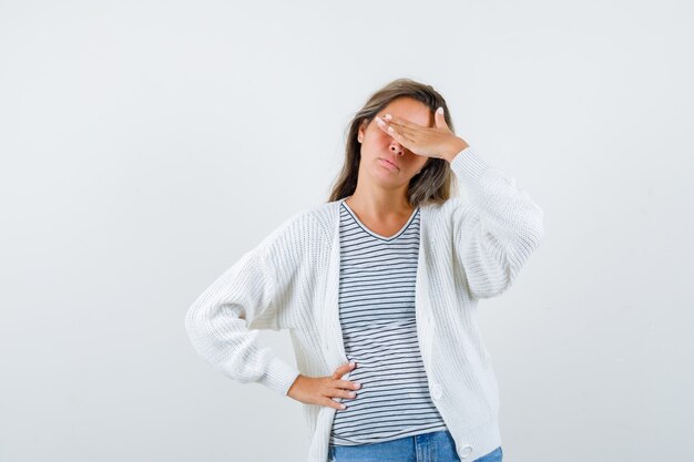 Mulher bonita no casaco, t-shirt segurando a mão sobre os olhos e parecendo oprimido, vista frontal.