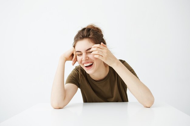 Mulher bonita nova alegre feliz com riso de sorriso do bolo que senta-se na tabela sobre o fundo branco.