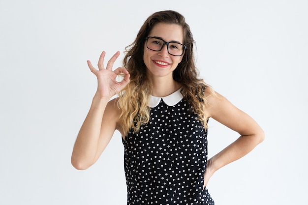 Mulher bonita nova de sorriso que mostra o sinal APROVADO e que olha a câmera.