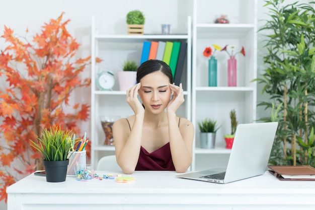 Mulher bonita nova que tem a dor de cabeça que trabalha no computador em casa