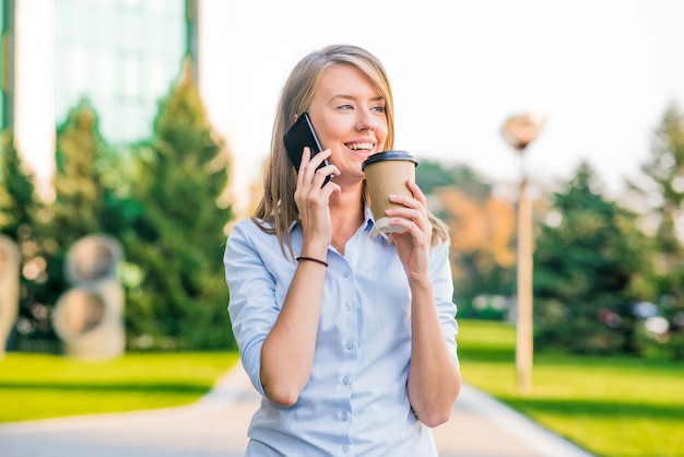 Mulher bonita que texting em um telefone esperto em um parque com um fundo verde