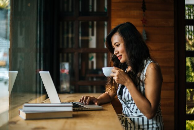 Mulher bonita que trabalha com o computador portátil no café café