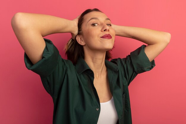 Mulher bonita satisfeita segurando a cabeça e olhando para a frente, isolada na parede rosa