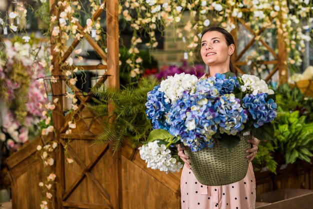 Mulher bonita, segurando o pote com flores em casa verde