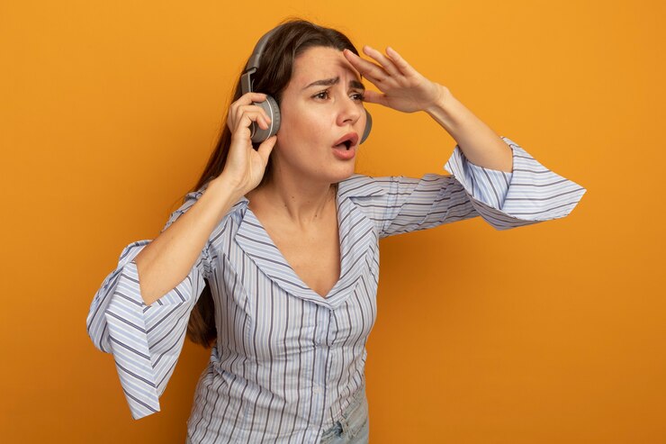 Foto grátis mulher bonita sem noção com fones de ouvido com a palma da mão na testa isolada na parede laranja