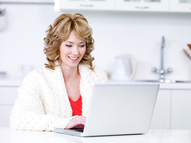 Mulher bonita sentada na cozinha e usando o laptop - dentro de casa