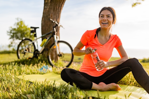 Mulher bonita sorridente bebendo água em garrafa fazendo esportes de manhã no parque