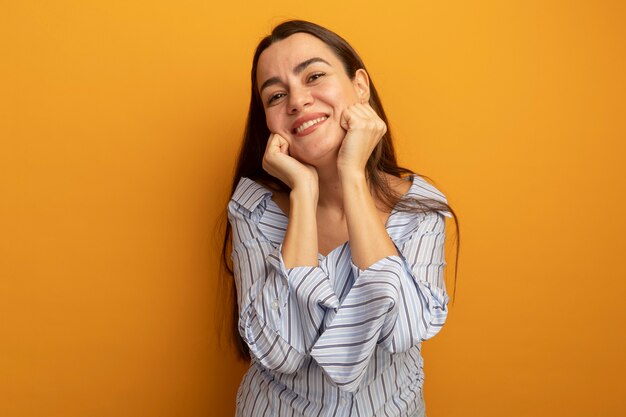 Mulher bonita sorridente coloca os punhos no rosto isolado na parede laranja