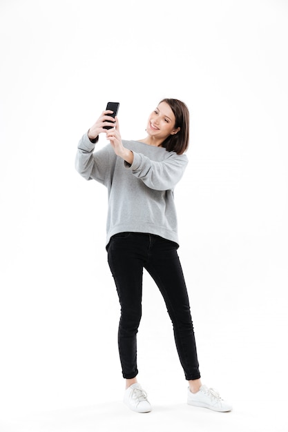 Mulher bonita sorridente em pé e tomando selfie no celular