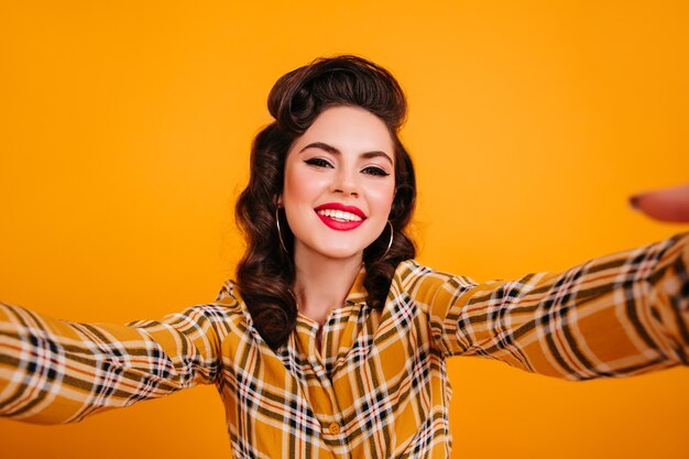 Mulher bonita sorridente tomando selfie em fundo amarelo. garota pinup feliz posando com camisa quadriculada.