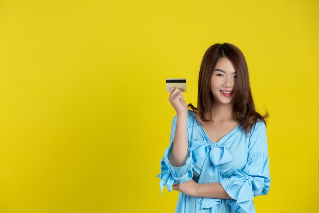 Mulher bonita sorrindo para a câmera e segurando um cartão de crédito na parede amarela
