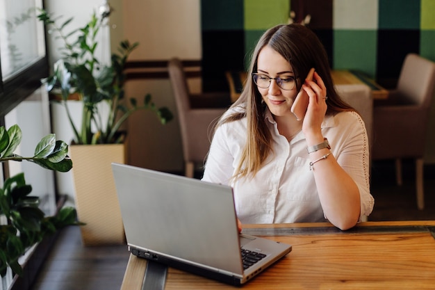 Mulher bonita trabalhando em seu laptop e telefone em um elegante restaurante urbano