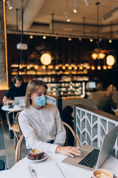 Mulher bonita usando máscara médica usando laptop para trabalhar