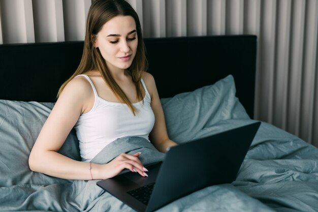 Mulher bonita usando seu laptop na cama pela manhã