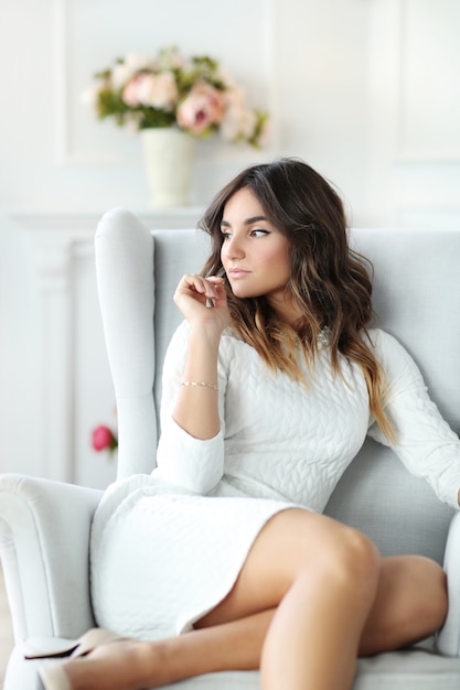 Mulher bonita usando vestido branco e sentado na poltrona branca