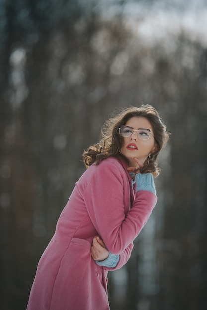 Mulher branca com uma jaqueta quente rosa brilhante em uma floresta de neve no inverno