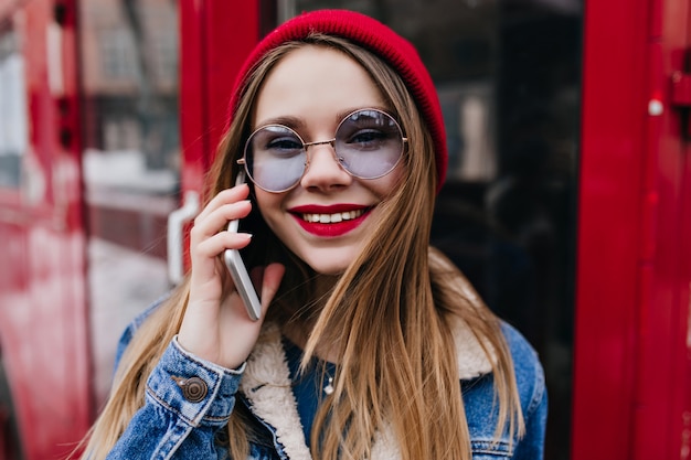 Mulher branca incrível em jaqueta jeans posando com o telefone vermelho