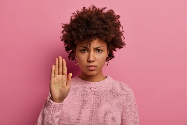 Mulher brava de pele escura com penteado afro, estende a palma da mão