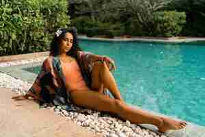 Foto grátis mulher bronzeada graciosa relaxando perto da piscina roupa elegante tropical plumeria flor nos cabelos