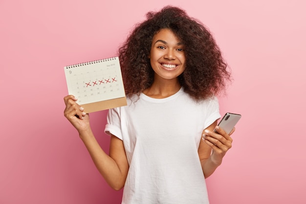 Mulher cacheada feliz segurando calendário de menstruação