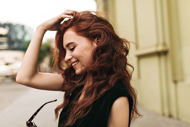 Mulher cacheada tirando óculos de sol e sorrindo