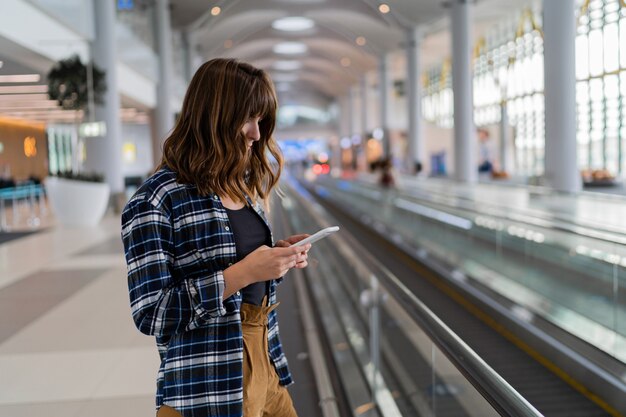Mulher caminhando pelo aeroporto usando seu dispositivo smartphone.