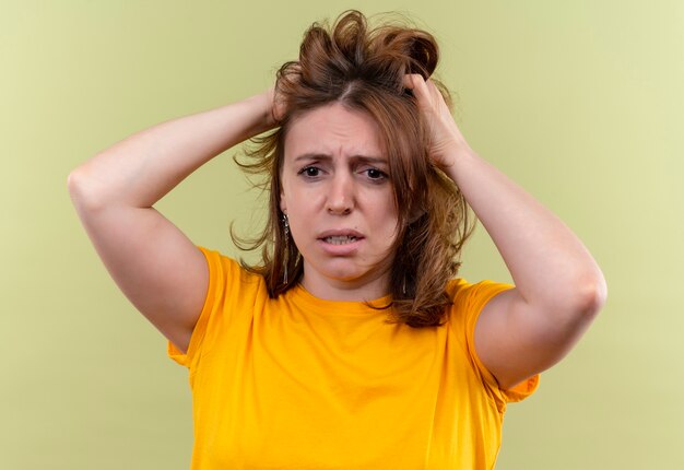 Mulher casual jovem e ansiosa segurando o cabelo em um espaço verde isolado